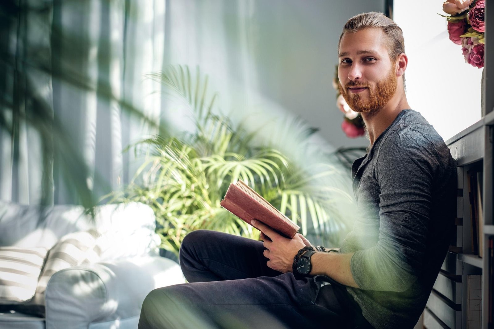 Homem belo sentado lendo livro sobre espiritualidade, vira o rosto sorrindo gentilmente